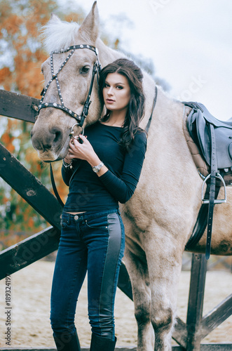 A beautiful brunette posing beside a slice on a rancorous ranch. Lifestyle Photo. Fashion photo. Autumn. Horseback riding