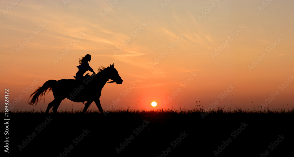 Horseback woman riding on galloping horse with red rising sun on horizon. Beautiful colorful sunset background with equine and girls silhouette horse hiking