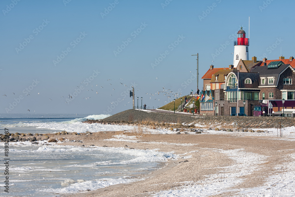 Winter landscape with Dutch beach covered with snow and view at lighthouse of fishing village Urk