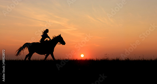 Fényképezés Horseback woman riding on galloping horse with red rising sun on horizon