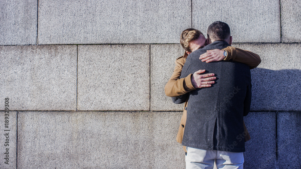 Young male couple embrace against a wall, with copy space