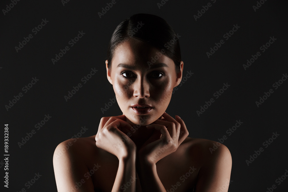 Beauty portrait of sexual caucasian woman with brown hair in bun posing at camera with beautiful look, isolated over black background