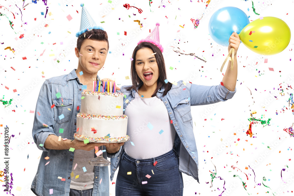 Teenagers holding a birthday cake and balloons with confetti streamers flying around them Teenagers holding a birthday cake and balloons with confetti streamers flying around them