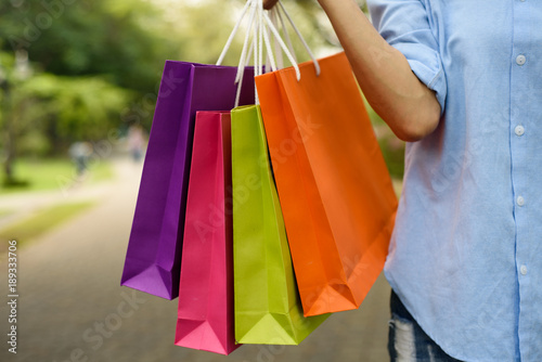 Asian woman holding shopping bags while walking in the park.