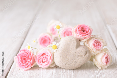 Pink roses and stone heart on rustic wooden background