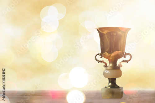Golden trophy on wooden table, bokeh and glitter background with copy space