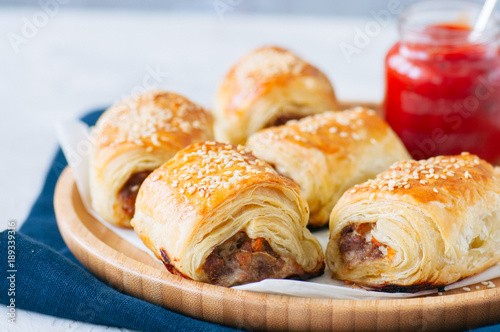 Beef and caramelised onion sausage rolls on a wooden plate with vegemite sauce