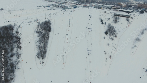 Aerial view: Skiers and snowboarders going down the slope in winter day. Skiers and snowboarders enjoying on slopes of ski resort in winter season.
