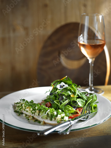 fish fillet with salad and a glass of rose wine on a wood table.