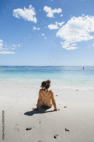 Young woman looks at the horizon sitting on a beach of Mauritius Island in the summer