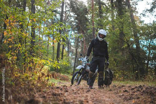 Man in dual sport helmet with backpack, enduro off road motorcycle on the forest road during sunrise. travel freedom concept