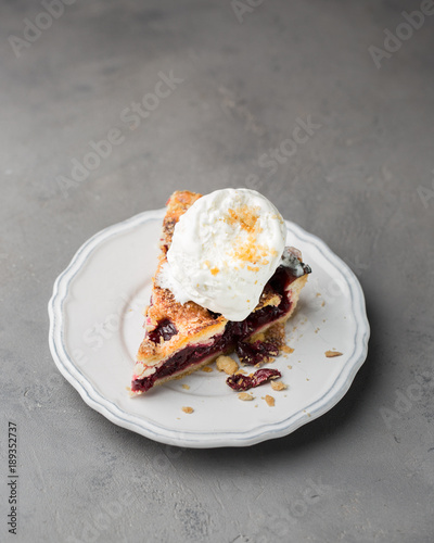 A piece of cherry pie with vanilla ice cream on a white vintage plate on a gray light concrete background. Copy Space. View blank space for text.