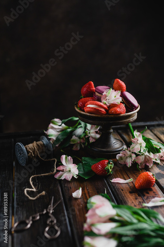 bowl with macarons and strawberries on wooden table with flowers