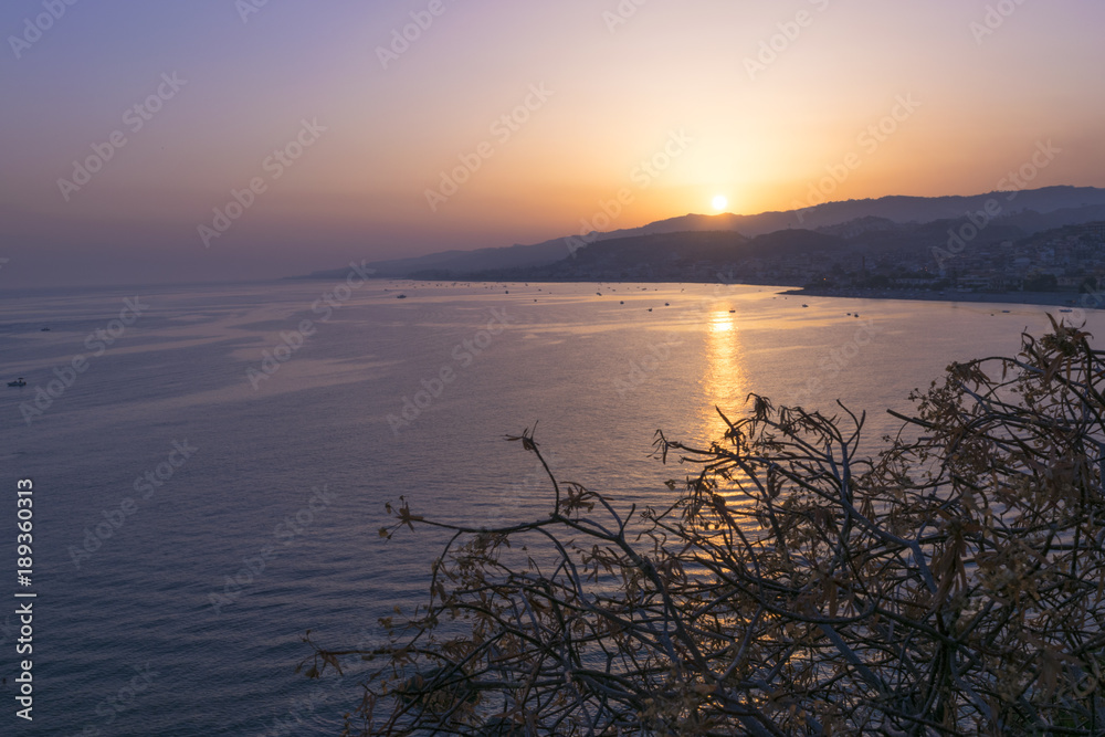 Panorama on the gulf with the purple sea and the boats moored on the fringe with the orange sun setting behind an arm of land in Borgia (calabria)