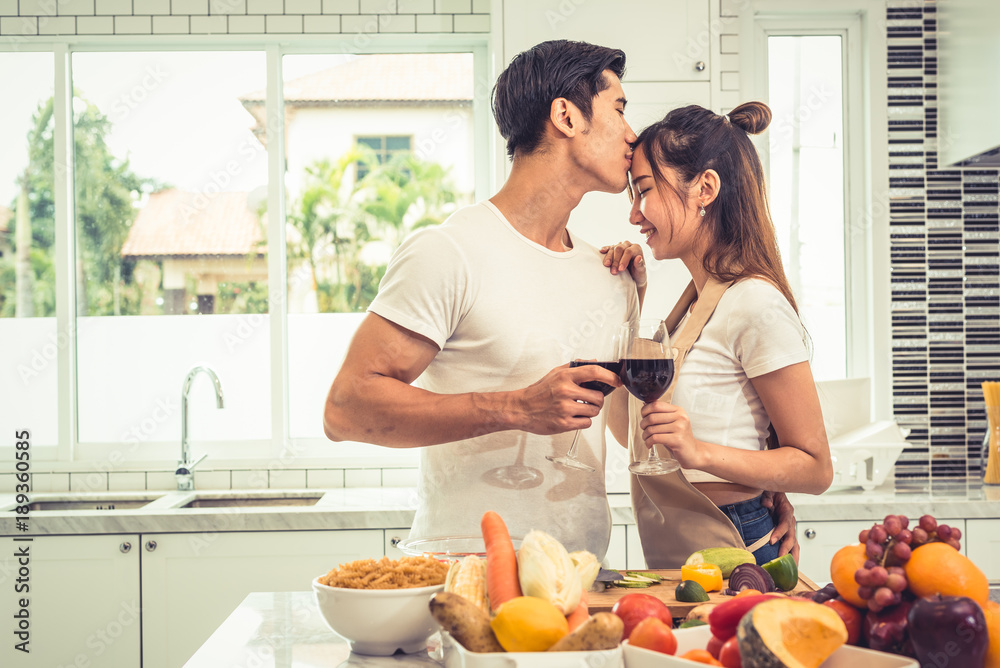 Asian lovers or couples kissing forehead and drinking wine in kitchen room at home. Love and happiness concept Sweet honeymoon and Valentine day theme