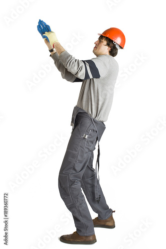 A young man in working grey clothes and orange hard helmet putting on a glove on white isolated background.