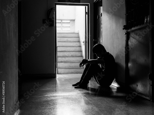 Silhouette of a sad young man sitting in the dark leaning against the wall with his back, The sun is in sorrow.