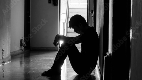 a sad young man sitting in the dark leaning against the wall with his back, The sun is in sorrow.