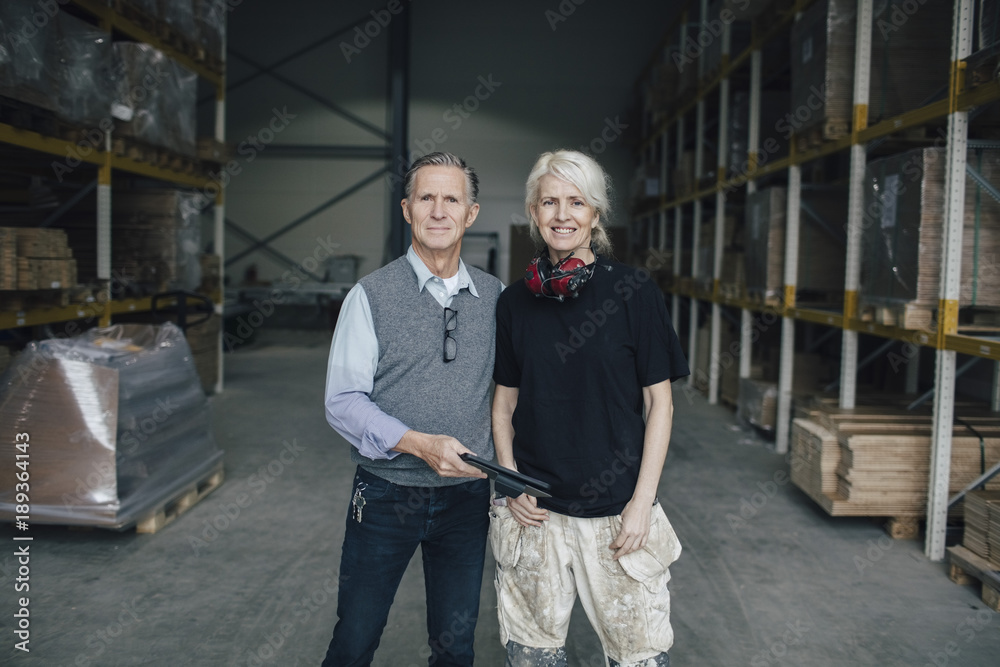 Portrait of smiling business colleagues standing against racks at industry Portrait of smiling business colleagues standing against racks at industry