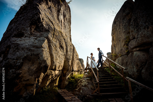 Glamour happy newlywed couple is standing on the wooden stairs between two rocks during the sunset. photo