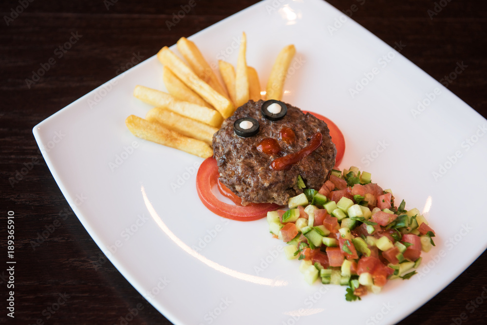 Funny meat cutlet face with french fries as hair and cutted vegetables for children menu Funny meat cutlet face with french fries as hair and cutted vegetables for children menu