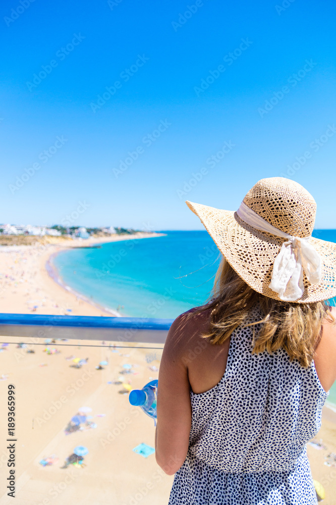 Woman wearing a hat, standing at viewpoint over, Albufeira beach on the Algarve, Portugal