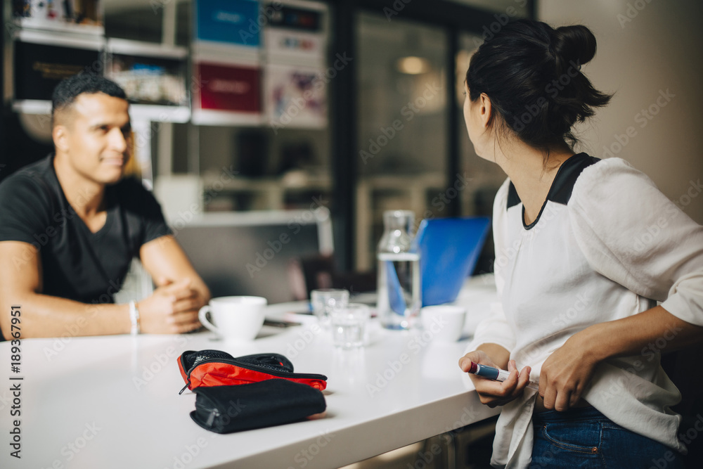 Businesswoman injecting insulin while talking to colleague at table Businesswoman injecting insulin while talking to colleague at table