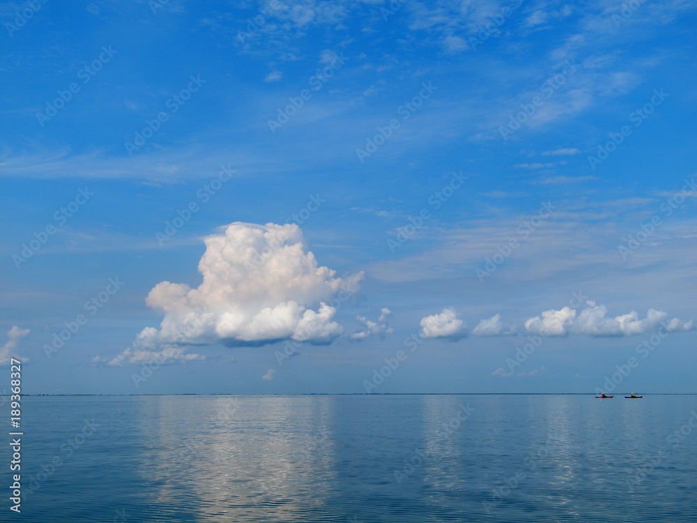 View of a beautiful calm blue sea and sky with clouds and two man in kayaks in foreground View of a beautiful calm blue sea and sky with clouds and two man in kayaks in foreground