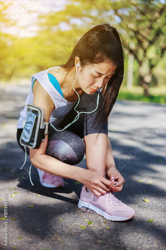 sporty woman tying shoelaces while listening to music with earphones from her smartphone in the park © geargodz