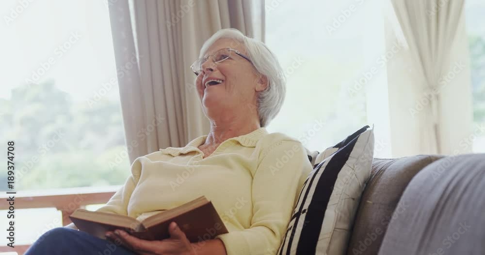 Grandmother seating on sofa and laughing while reading book Grandmother seating on sofa and laughing while reading book