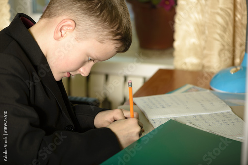 The boy works in his office on a personal computer.He writes a letter at the writing desk...