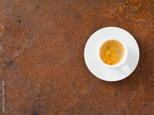 black frothy coffee with foam in white cup with plate on rusty metal table, top view, empty space for text