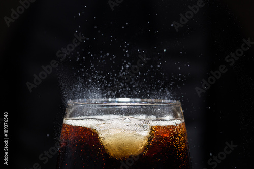 A glass of cola beverage with a salt. On a black background.