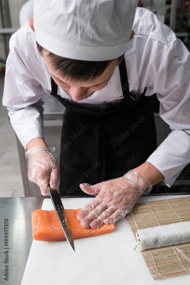 Chef cuts salmon or trout when preparing philadelphia sushi rolls.