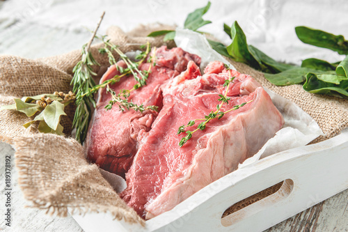 Cuts of beef for grilling on a wooden cutting Board with spinach, rosemary and Provencal herbs for the marinade in a rustic style.
