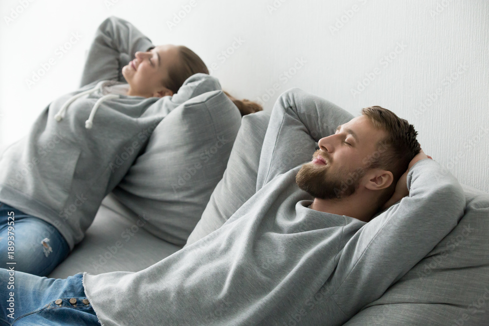 Fototapeta premium Happy young couple relaxing on comfortable soft couch cushions together at home, smiling man and woman enjoying rest nap on cozy new sofa in living room breathing fresh air feeling totally relaxed