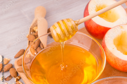 cup of honey, apples, wooden spoon and walnuts and almonds on light wooden background