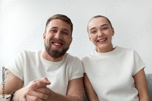 Smiling young couple with happy faces looking at web camera, man and woman making videocall to distance friend by skype, funny vloggers recording videoblog or video message, webcam view portrait