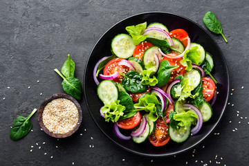 Healthy vegetable salad of fresh tomato, cucumber, onion, spinach, lettuce and sesame on plate. Diet menu. Top view.
