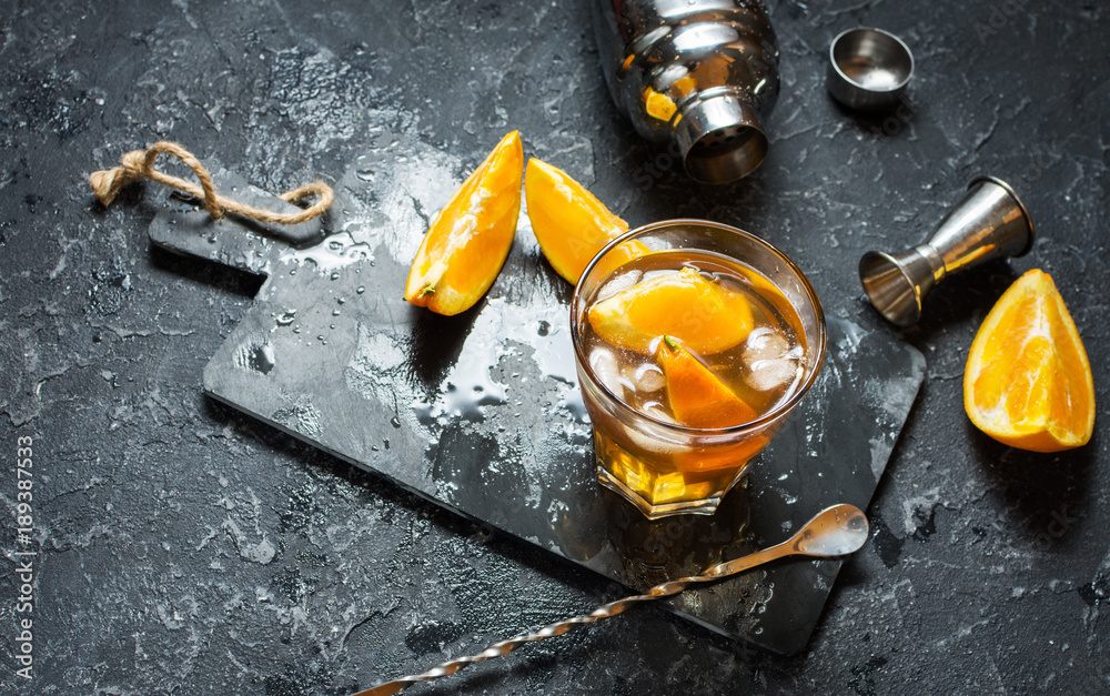 A glass of Negroni cocktail with orange and lemon. Alcoholic drink with rum and vermouth on dark stone table. With space for text