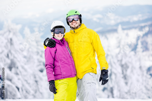 Portrait of a young and happy couple snowboarders in colorful sports clothes standing together on the snowy mountains