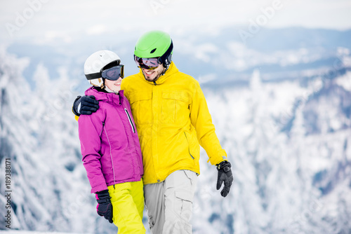 Portrait of a young and happy couple snowboarders in colorful sports clothes standing together on the snowy mountains