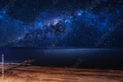 Night starry sky over the beach with a pier.