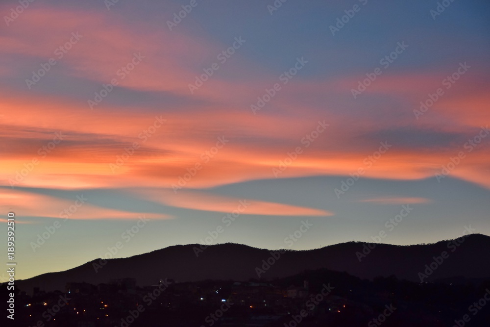 Tramonto con nuvole arancioni e rosa sulla collina