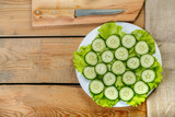On a wooden table in a white plate lie the cut cucumbers for a salad and a knife