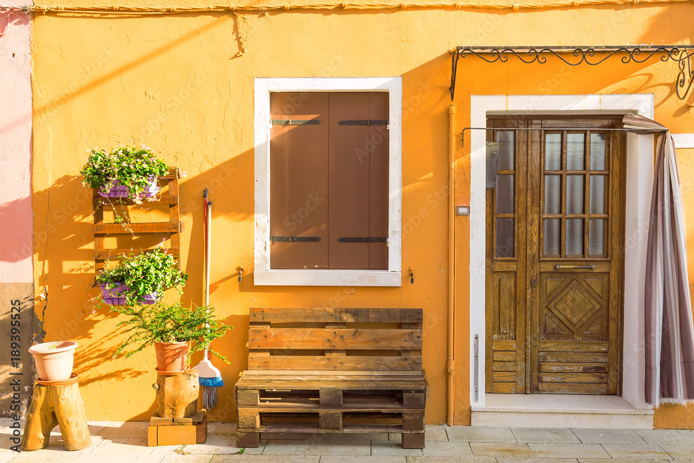 Obraz premium Yellow house with flowers and bench. Colorful houses in Burano island near Venice, Italy. Venice postcard. Famous place for european tourism and travel