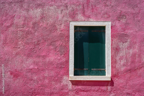 Window with closed green green shutter on bright pink wall. Italy, Venice, Burano island.