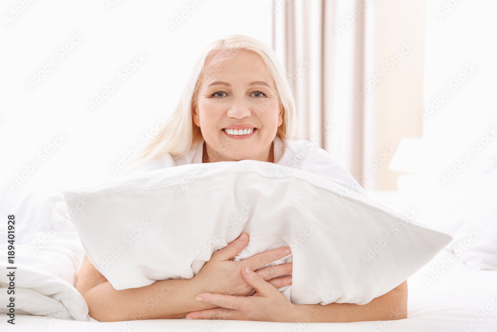 Senior woman hugging white pillow at home Senior woman hugging white pillow at home