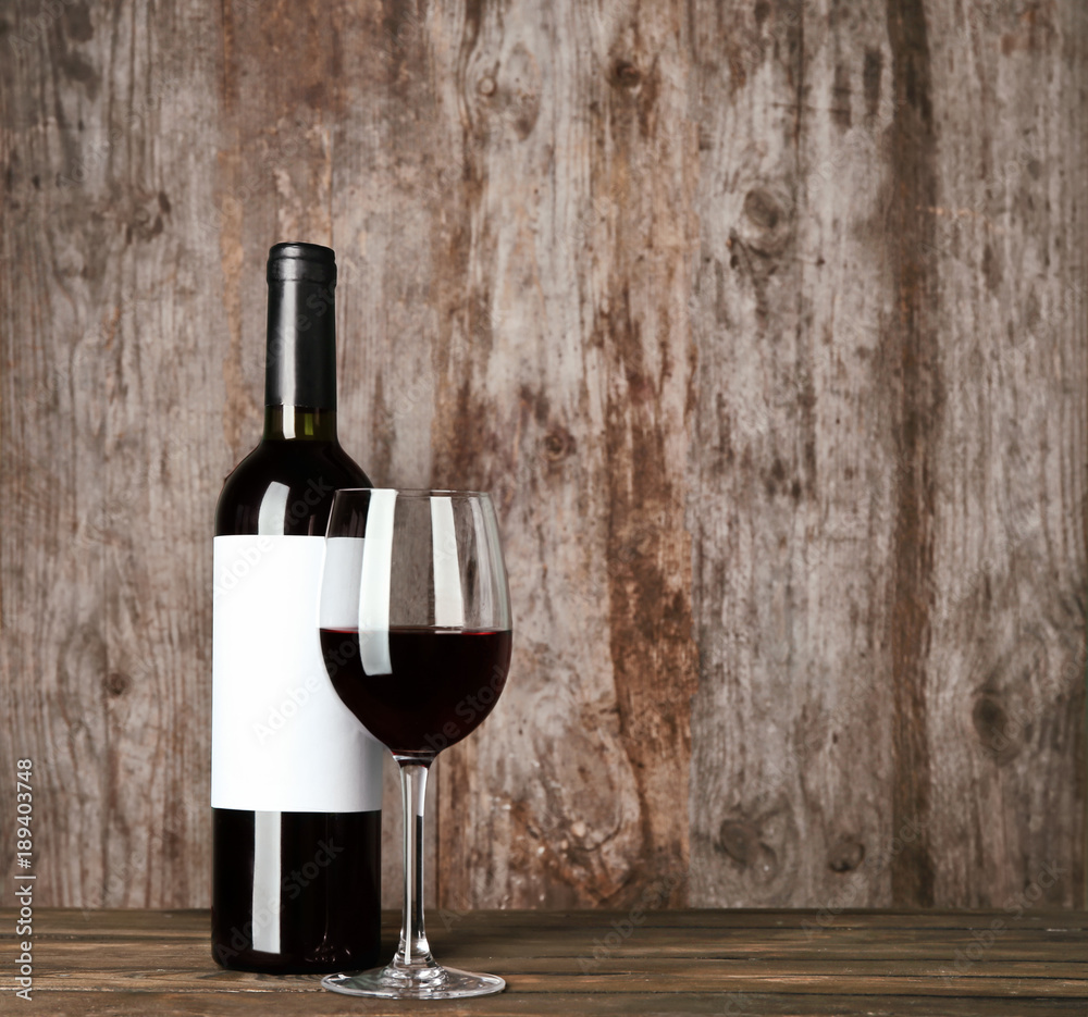 Glass of red wine and bottle with blank label on wooden table. Mock up for design