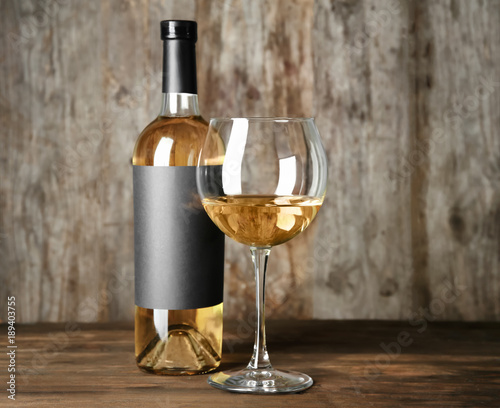 Glass of white wine and bottle with blank label on wooden table. Mock up for design